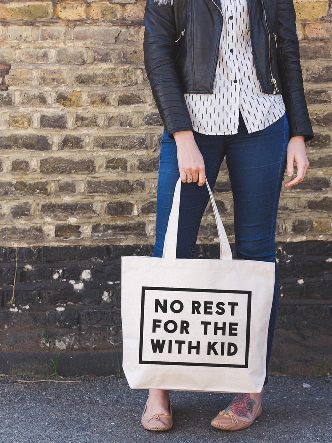 a model holding a large natural canvas tote bag bearing the words no rest for the with kid
