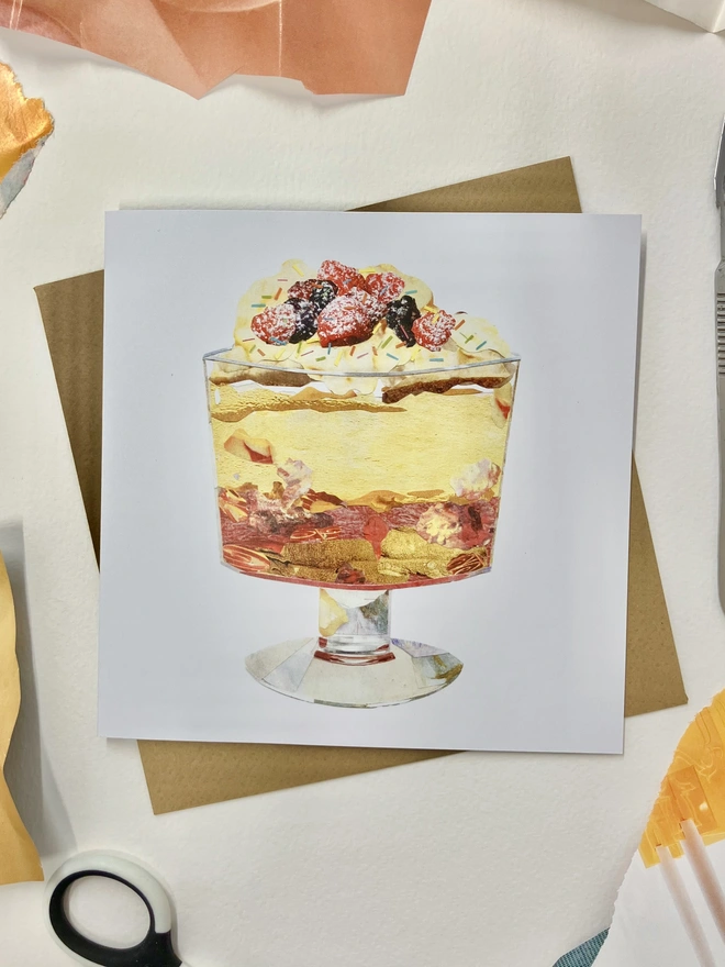 Collage of a birthday trifle on a greetings card with an envelope on a background with collage materials around.