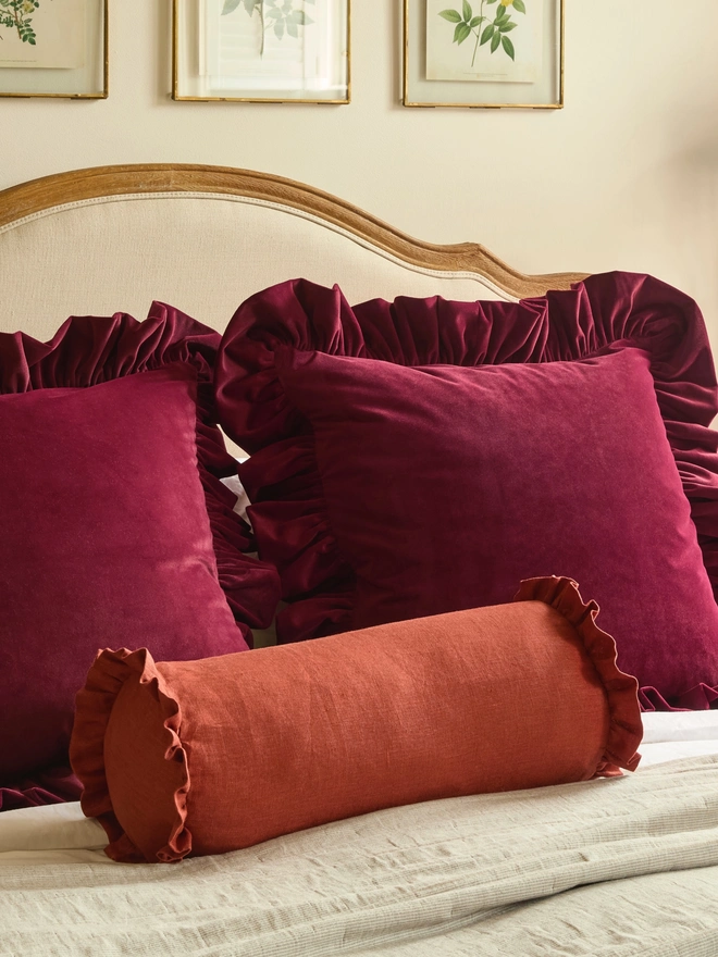 Kika Bespoke handmade rust classic linen bolster cushion on bed with velvet ruffled cushions