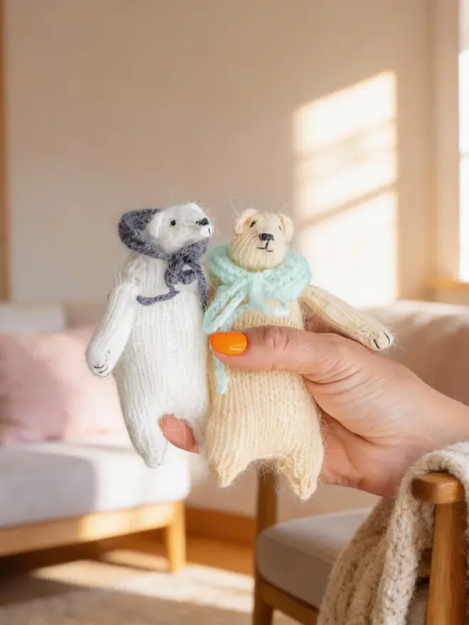 Ottilie The Bear Cashmere Figure, a pair of cashmere bears held by a person against a living room backdrop. 