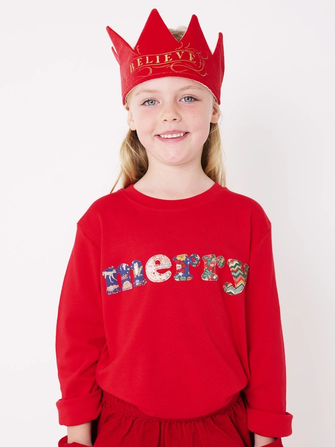 a 5 year old wearing a red christmas cotton t-shirt with the word merry hand cut from festive Liberty prints and appliquéd on the front