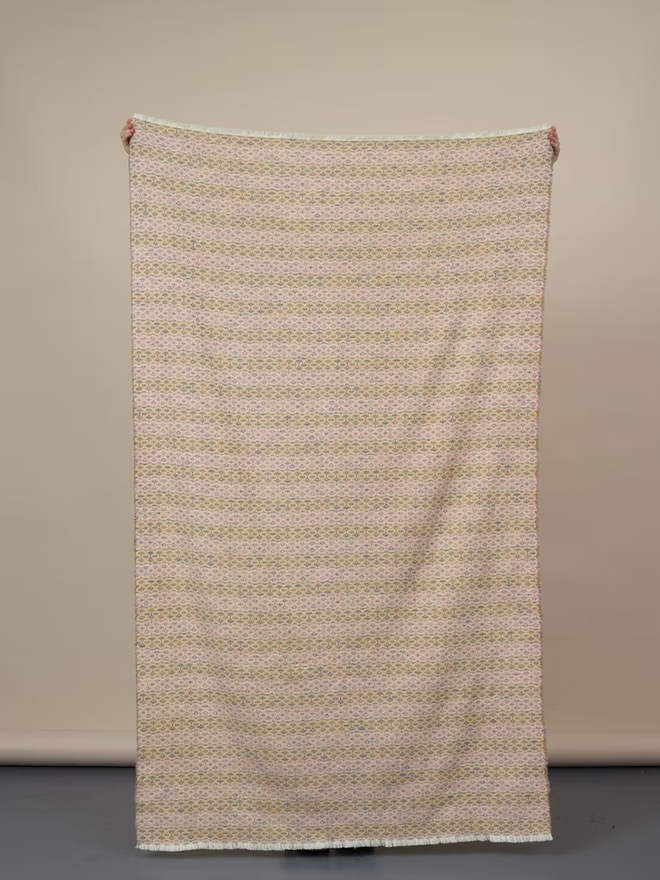 cairmeal lambswool blanket. a pink and brown blanket against a plain wall.