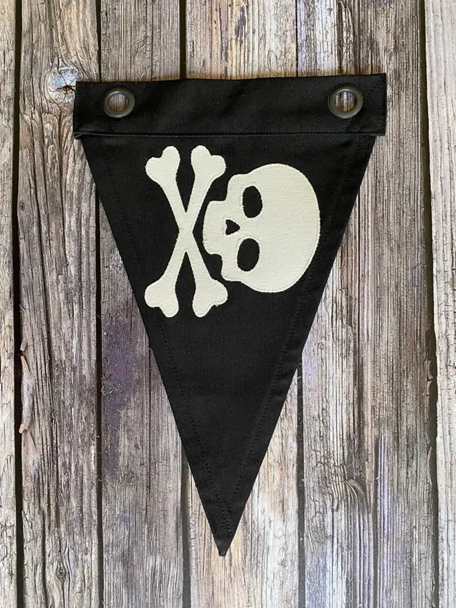 a black oennant flag with an ivory skull and crossbones stiched on, laying on a wooden floor