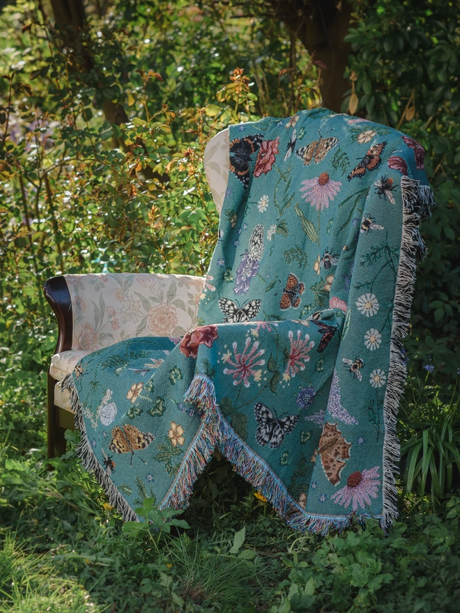 'Pollination Bloom' Recycled Cotton Blanket seen on a chair outside.