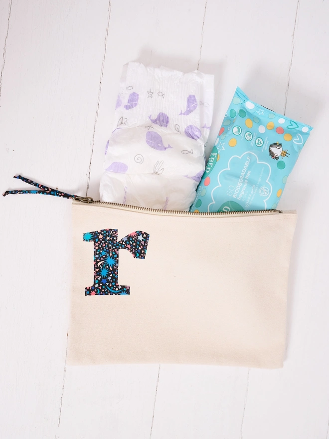 a natural zip up pouch used as a nappy bag personalised with a liberty print initial on the front in the corner