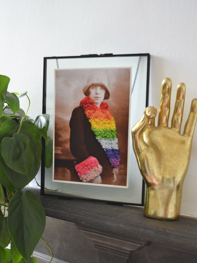 Print of woman wearing embroidered rainbow coloured trim coat framed on mantlepiece