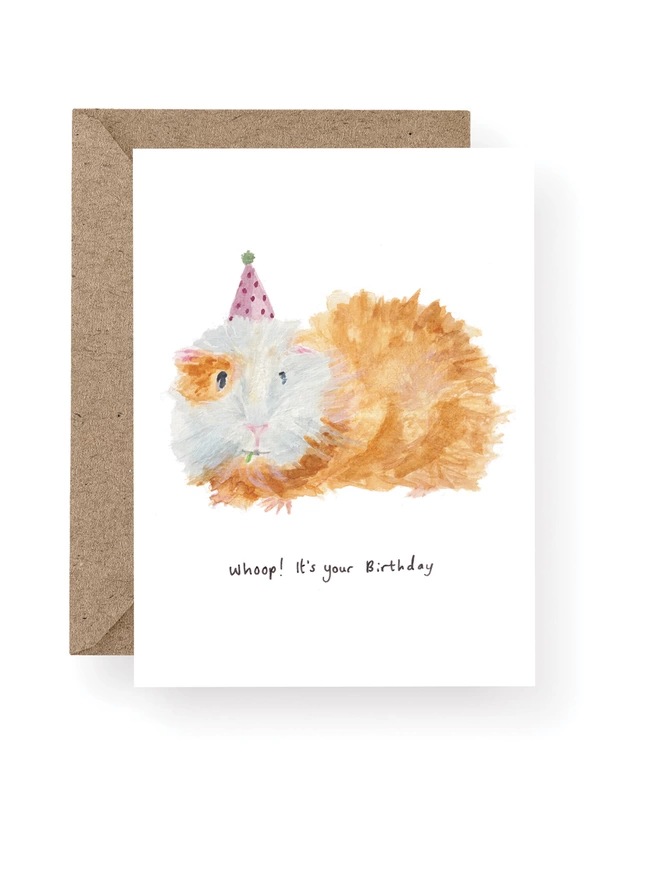  Guinea Pig Birthday Card, Card Has a White Base With Hand Painted Guinea Pig Wearing A Party Hat.  Sitting On A Recycled Brown Kraft Envelope.  There Is Black Handwritten Text Underneath The Guinea Pigs Which Reads ‘ Whoop It’s Your Birthday’