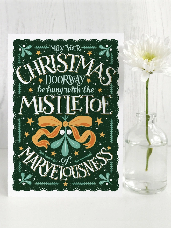dark green and orange christmas mistletoe card with white hand lettered quote