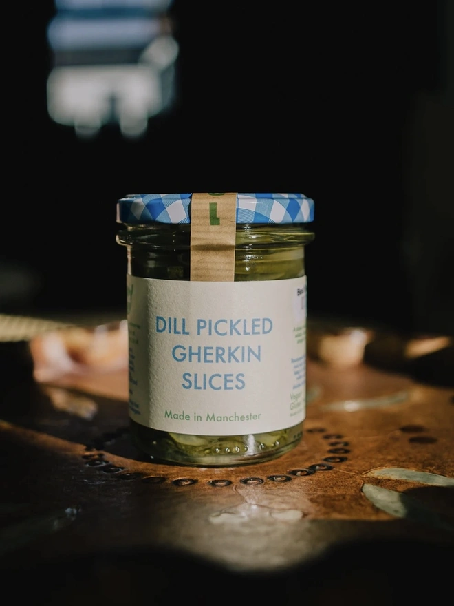 Jar Of Dill Pickled Gherkin Slices, jar of gherkin slices with a blue lid on a decorated plate. 