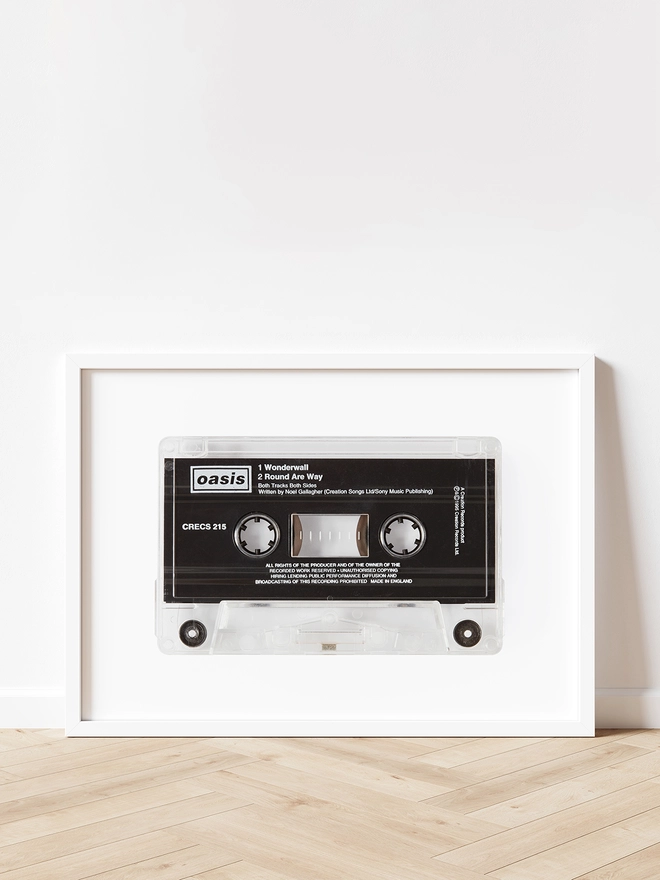 oasis wonderwall cassette tape print. framed print propped up against white wall on wooden floor.