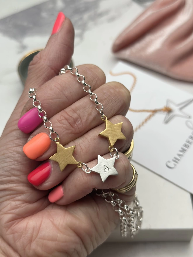 3 chunky star charms hang horizontally from a sterling silver chain.  a personalised silver star hangs in the middle with gold stars on each side