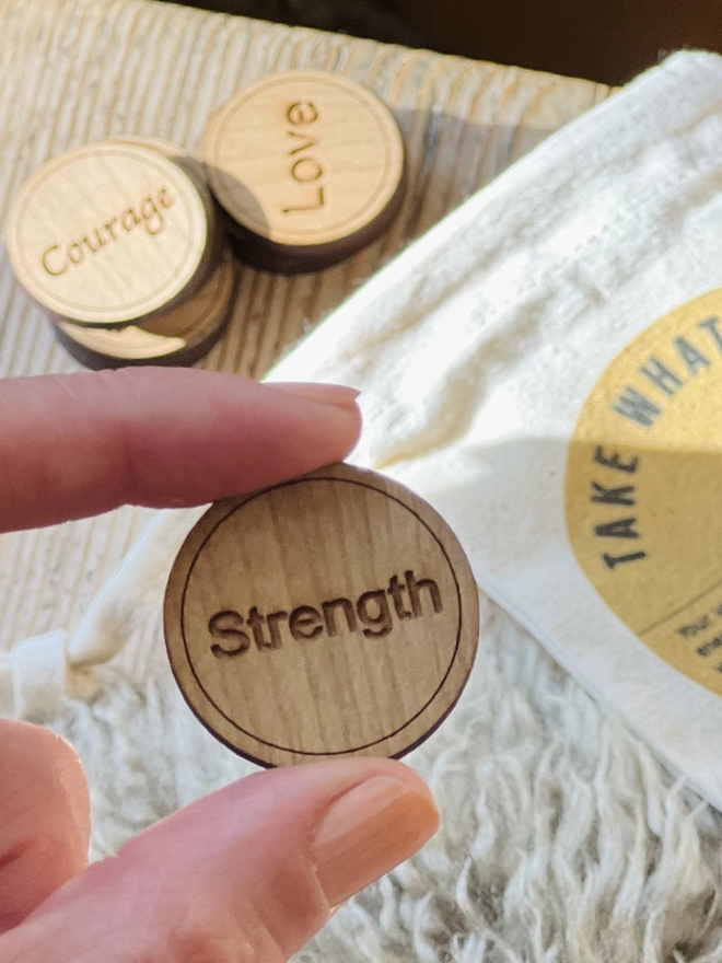 Close up shot of a token which reads "Strength" being held by a index finger and thumb 