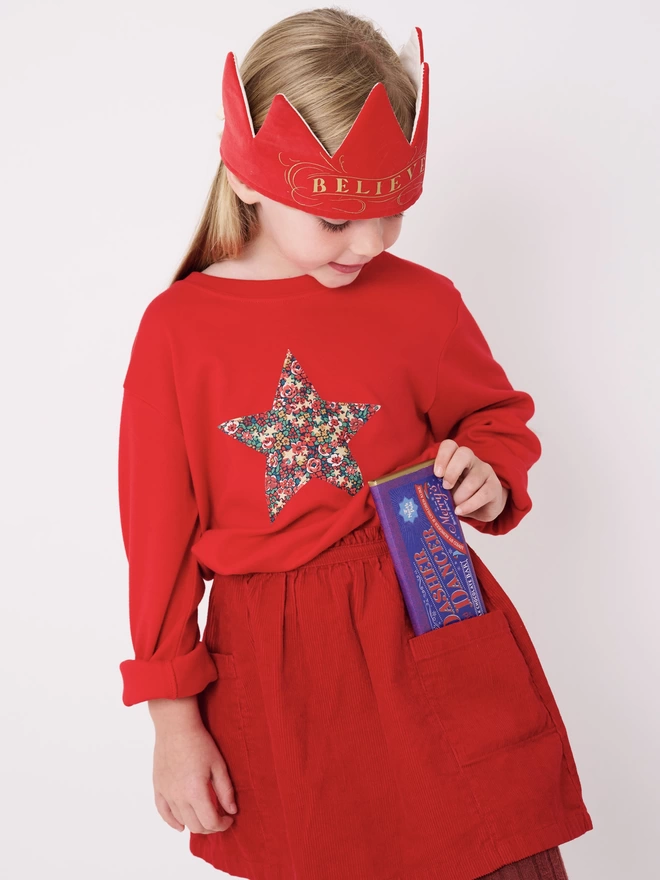 A girl wearing a red t-shirt with a Liberty print floral star sewn on the front