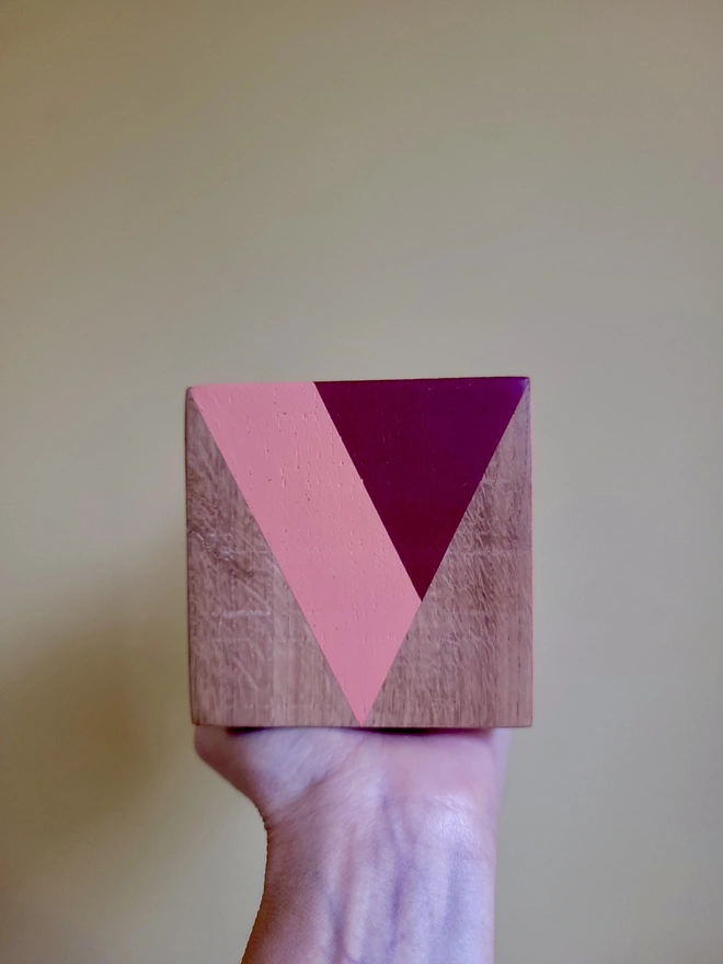 Wood cube tealight holder painted red and pink triangle V held against a yellow background