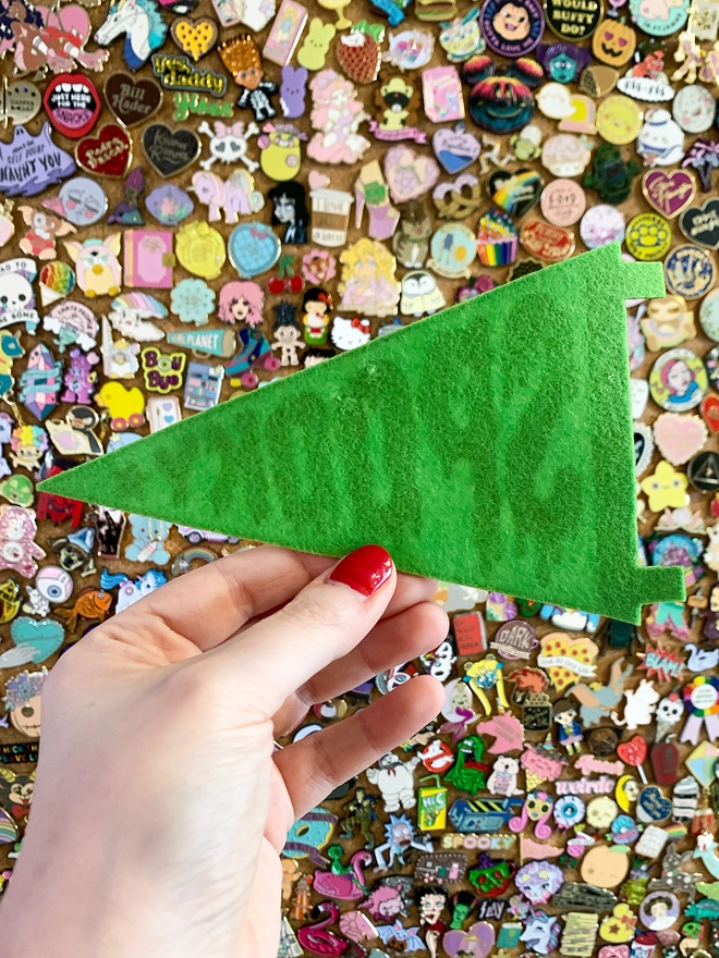 image shows a hand holding a green felt pennant. it only shows the back of the pennant which is plain green, with the print from the other side showing through slightly.