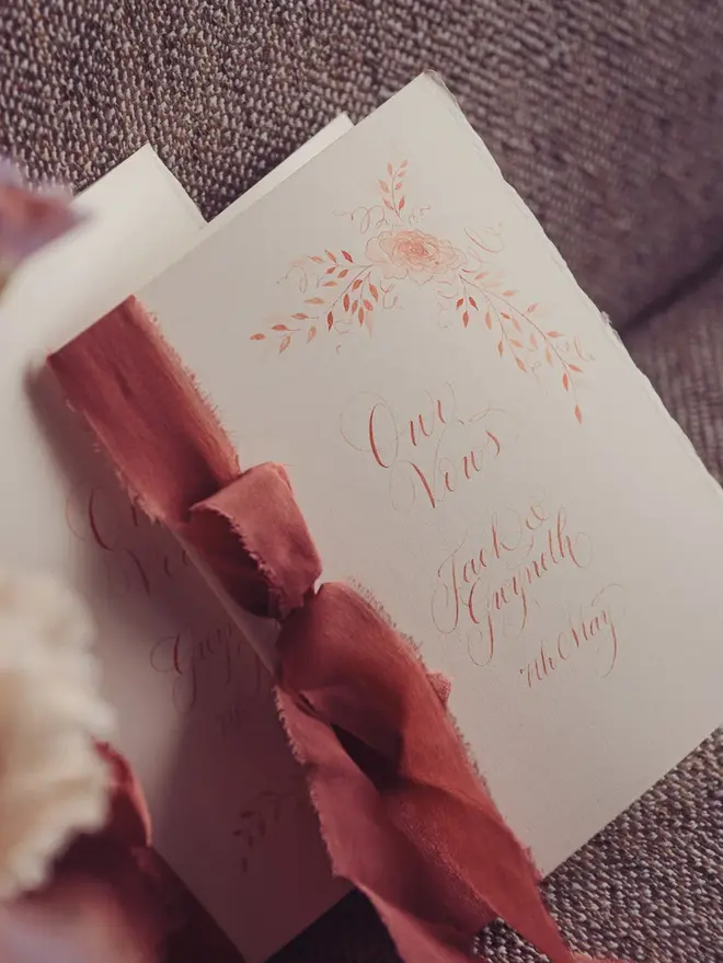 personalised calligraphy wedding vow booklet. white booklet with rust red calligraphy on cover.