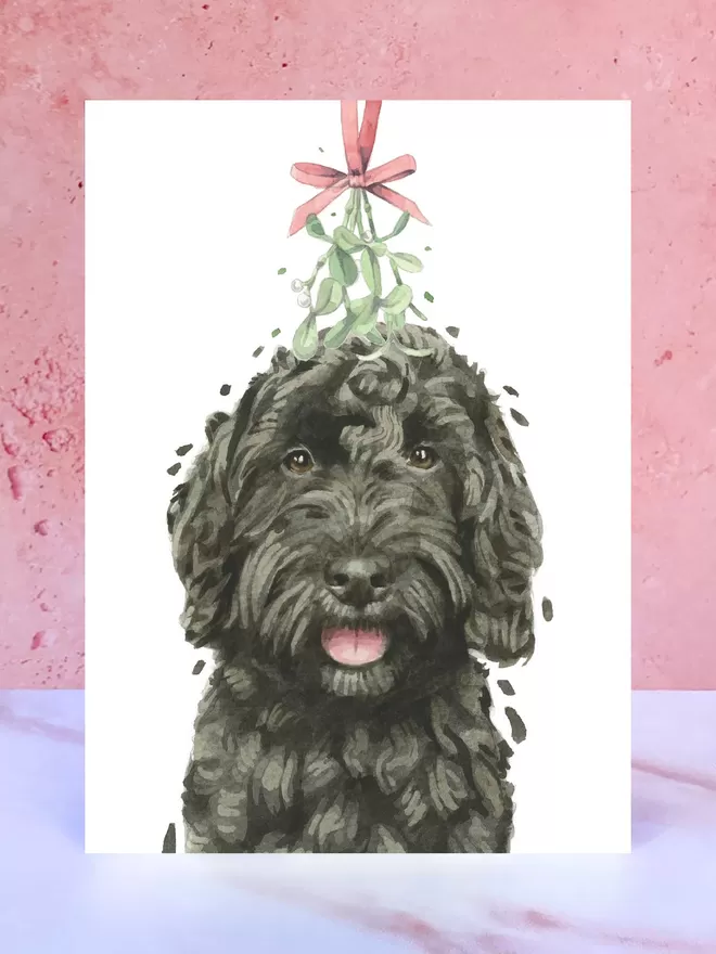 A Christmas card featuring a hand painted design of a Black Cockapoo, stood upright on a marble surface.