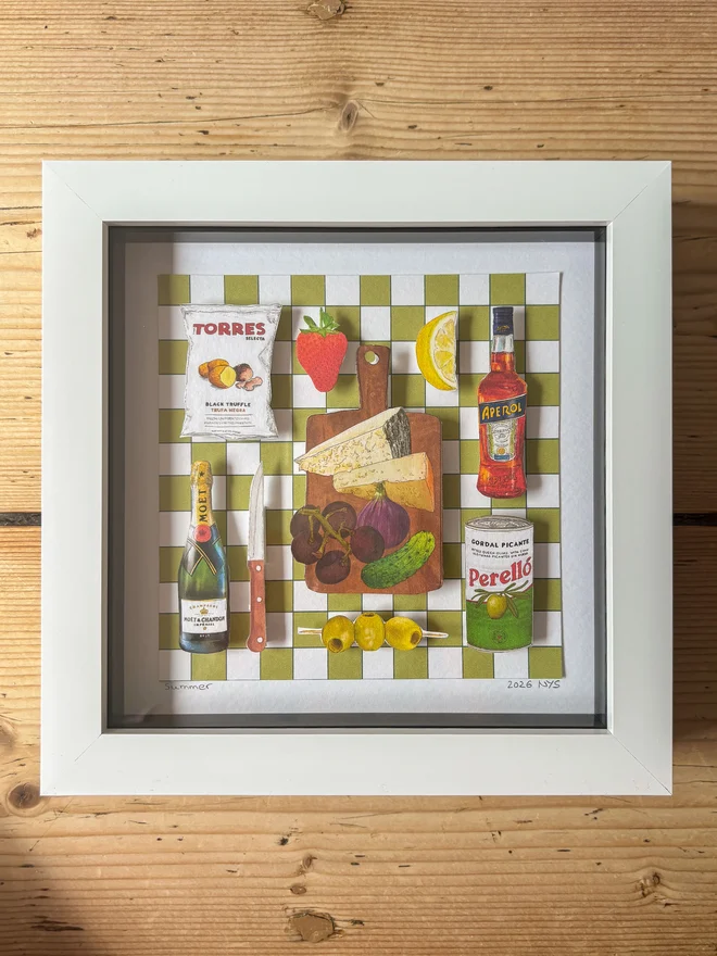 Illustrated 3D paper collage in a white frame showing picnic cupboard staples on a green white background, on a wooden surface
