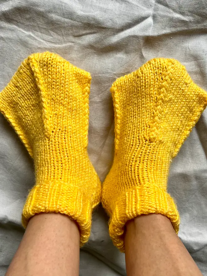 Duck Feet Socks, a person wearing a pair of yellow duck feet socks on a white cloth surface. 