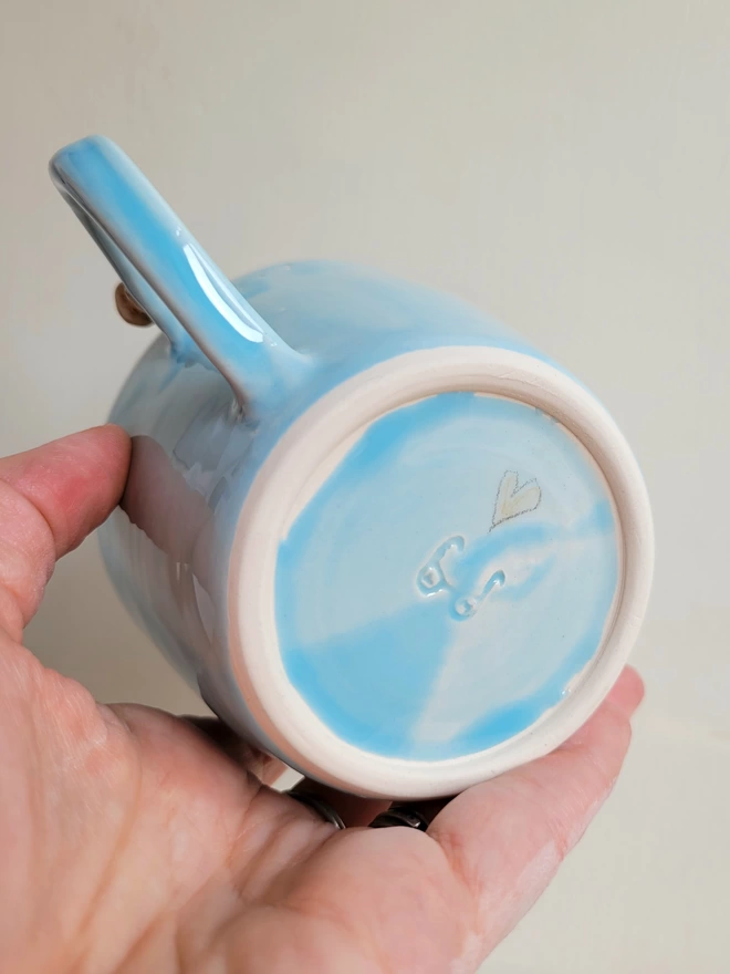 Handmade pottery blue cup base with hand painted love heart held in a hand