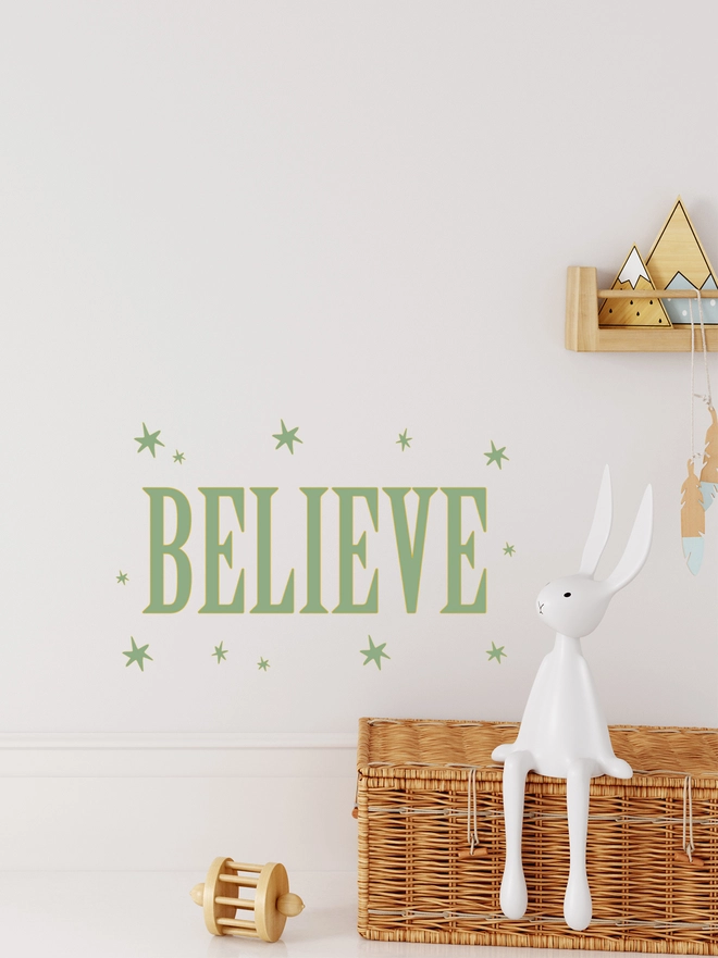 believe wall sticker in green  with green stars surround wording above a cot