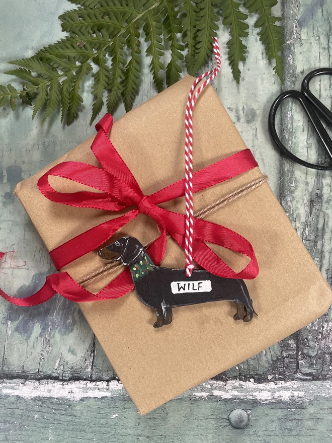 A dachshund Christmas decoration personalised with the dogs name, laid on a gift