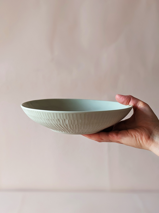 Porcelain Pasta Bowl in Pale Rockpool Green with hand carved scalloped details being held in a hand  