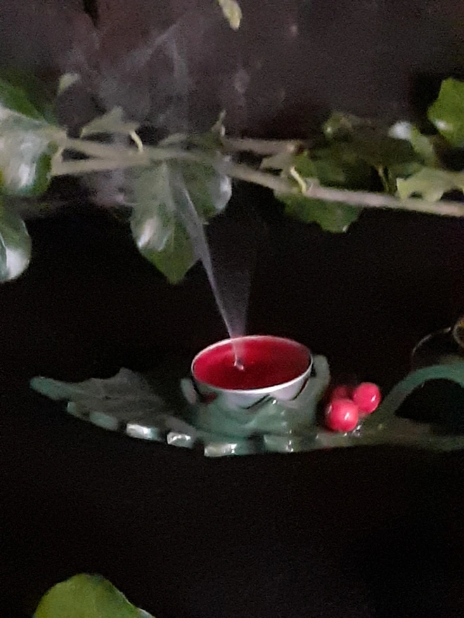 Green ceramic holly leaf candle holder with red berries and a recently extinguished tealight, with smoke curling above the wick.