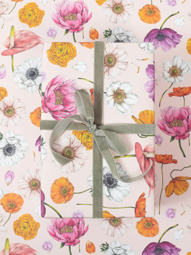 floral brights floral gift wrap sheet. a box wrapped in pale pink illustrated floral gift wrap with a green ribbon.