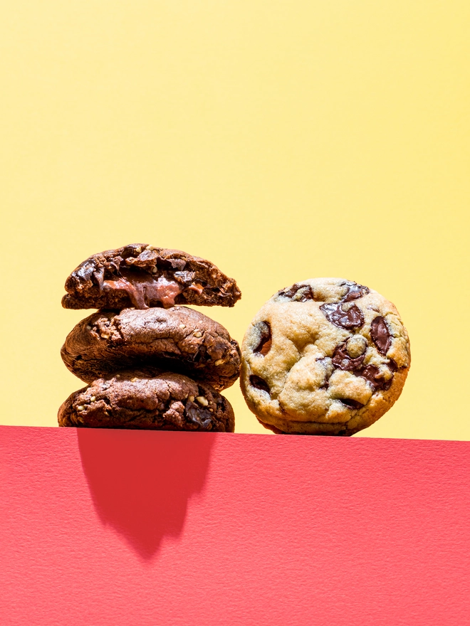 Cookie Selection (Box Of 4), biscuits standing on a red surface against a yellow backdrop. 