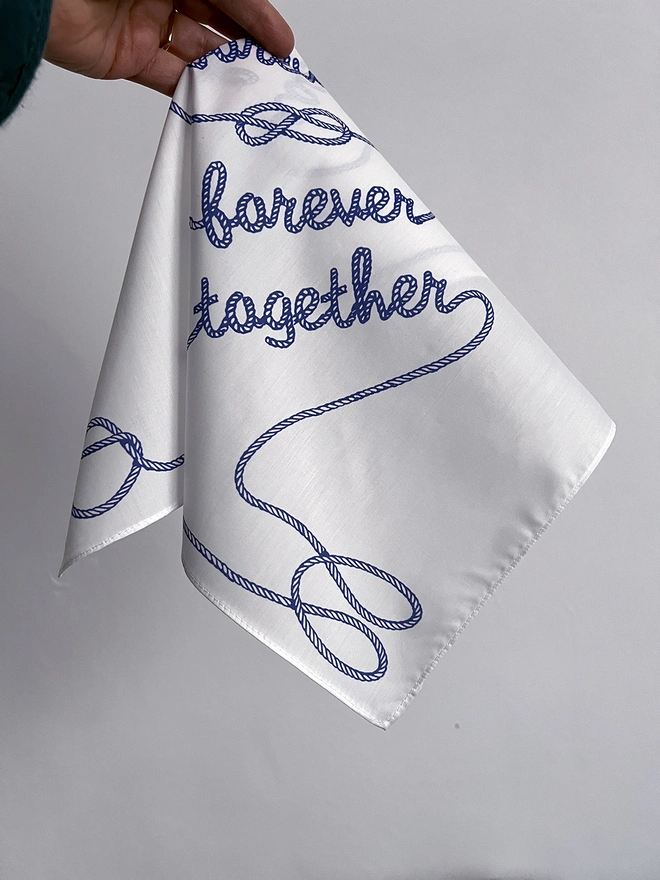 A Mr.PS Together Forever Handkerchief held by a white hand in front of a white wall