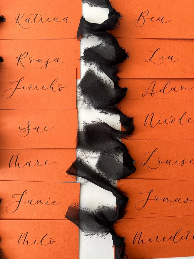 Personalised Calligraphy Rust Orange Place Card, orange place cards with black chiffon ribbons grouped together on a white surface. 