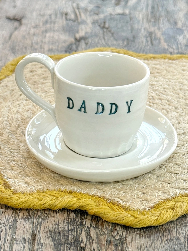 Espresso cup and saucer with DADDY emblazoned on the side with shimmering blue lustre detailing. Sat on a farmhouse style wooden table