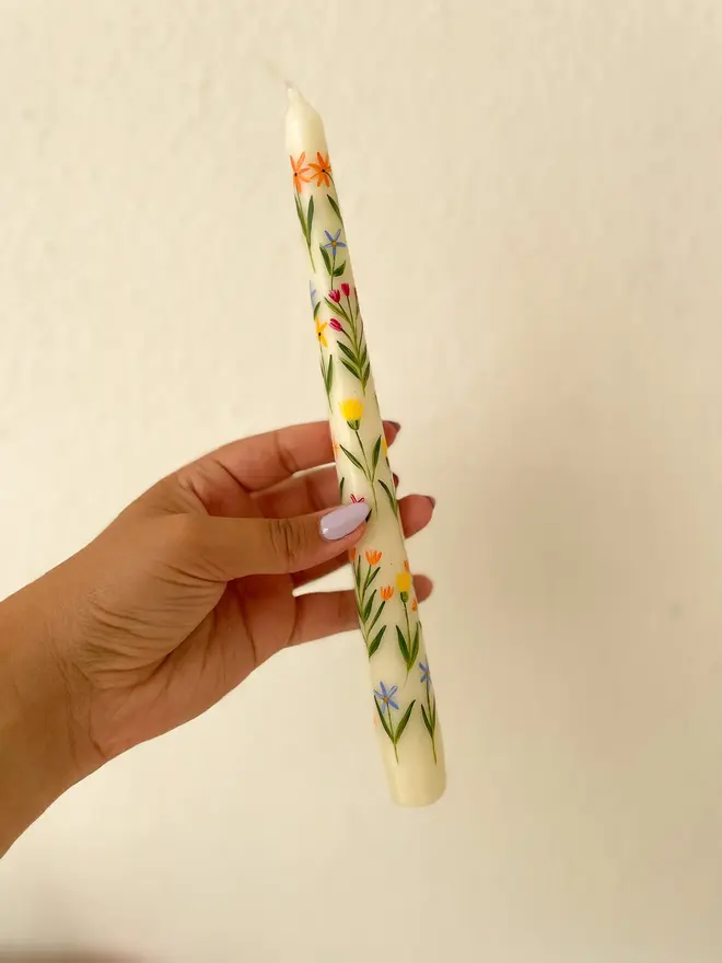 Summer Field Flowers Candle, a person holding the summer candle against a plain background. It's floral design can be seen wrapping around it. 