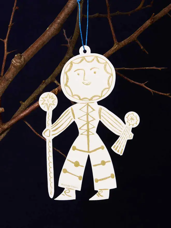 Decorative Sun Folk ornament hanging from a branch against a dark background