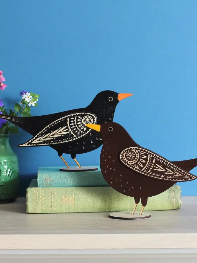 Standing Wooden Female Blackbird, black wooden bird standing on a book on a wooden platform. 