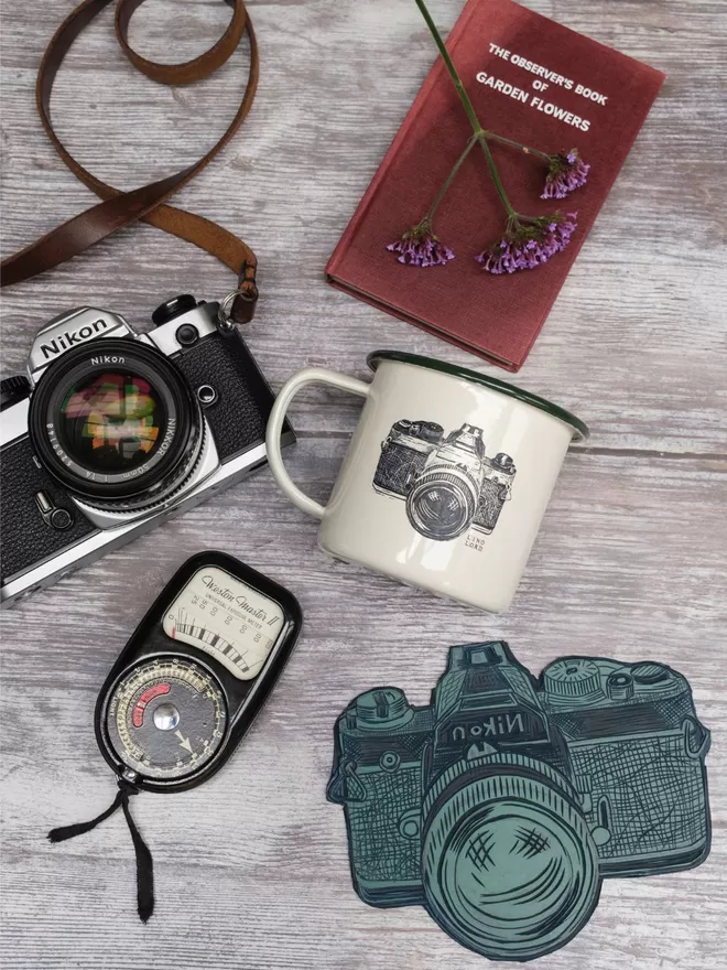 Picture of a Cream Enamel Mug with a Green Rim with a Camera design etched onto it, taken from an original Lino Print
