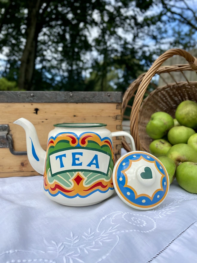 Cream vintage teapot, hand painted with a fairground design in green, blue, yellow and red. ‘Tea’ is painted in a banner across the centre.