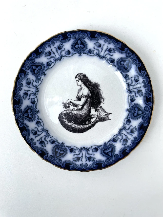 vintage plate with an ornate border, with a printed vintage illustration of mermaid in the middle 