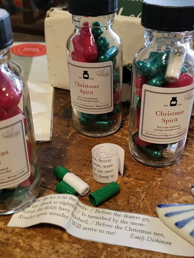 Glass bottle containing red and green Christmas Spirit poetry pills printed on banana paper