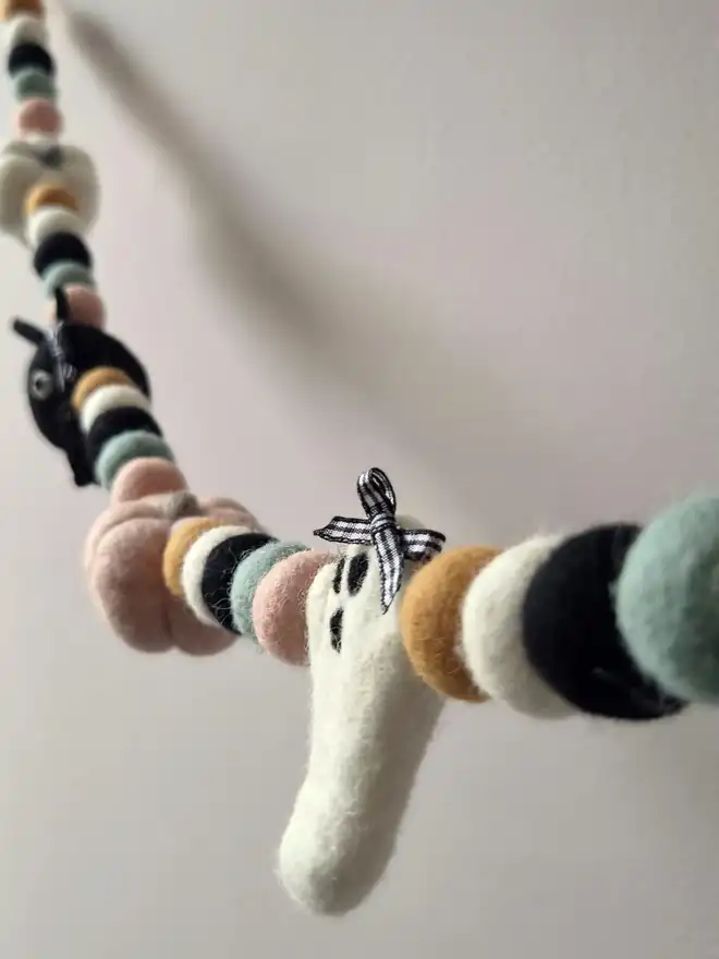 An ivory ghost with a black and white gingham bow, hung in a Halloween garland.
