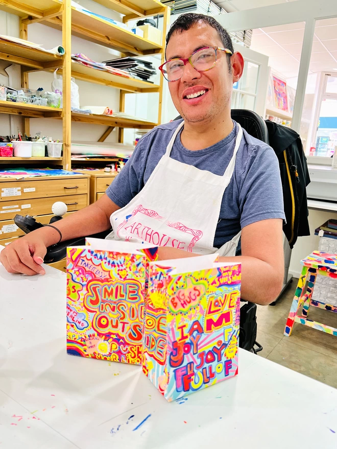 happy artist holding bright colourful packaging for charity full of joy white chocolate buttons 