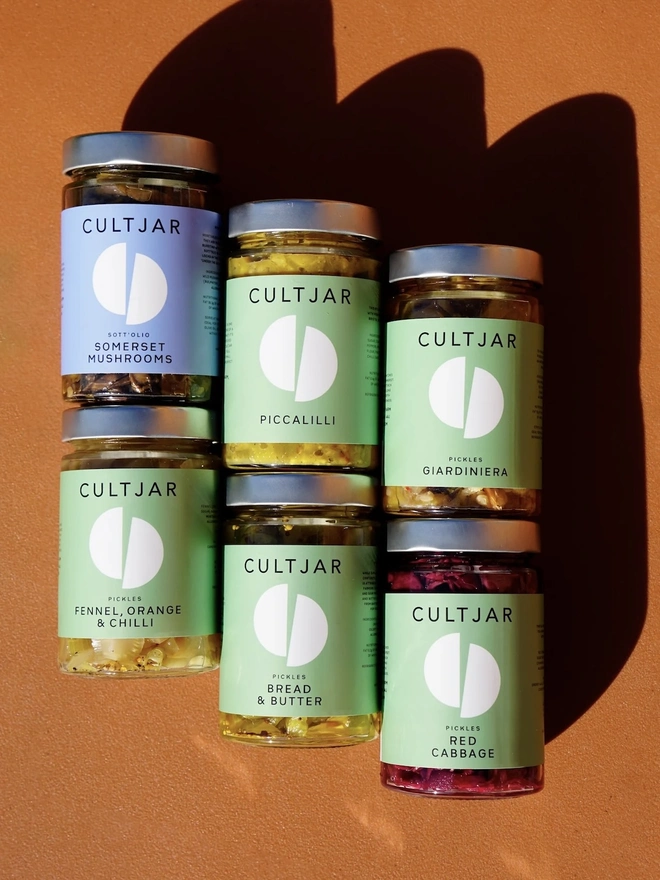 Premium Pickle Gift Pack (Set Of 6), a group of six pickle jars sitting on an orange surface. 