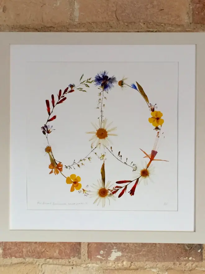 Pressed Wildflower Peace Sign Print, a wildflower peace sign print sitting framed against a brick wall. 