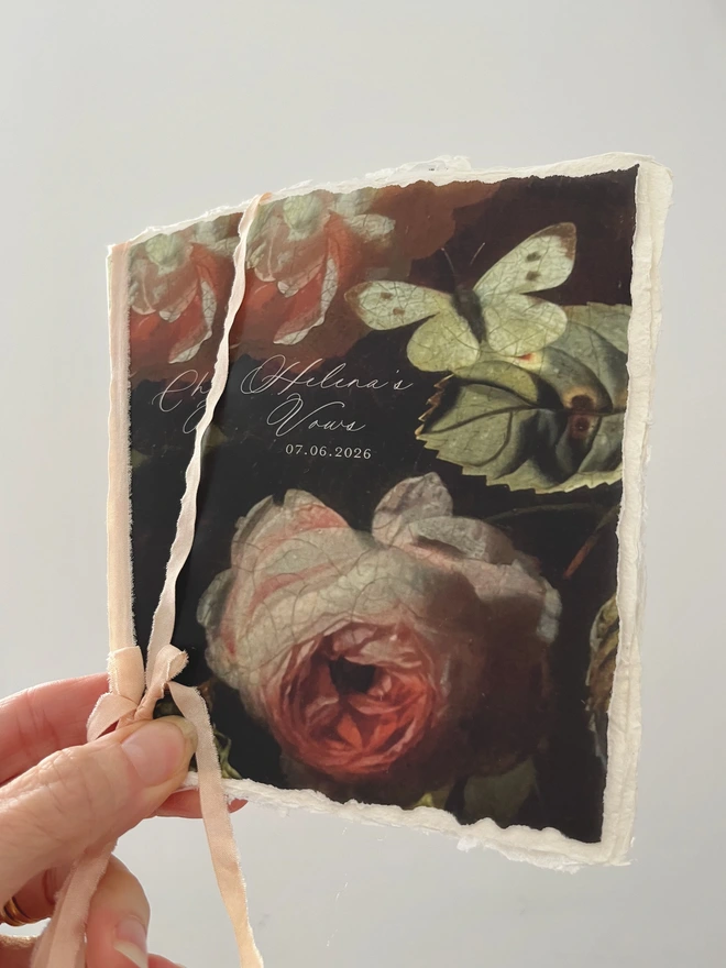 Close of photo of the Butterfly and Roses vow booklets photographed being held.