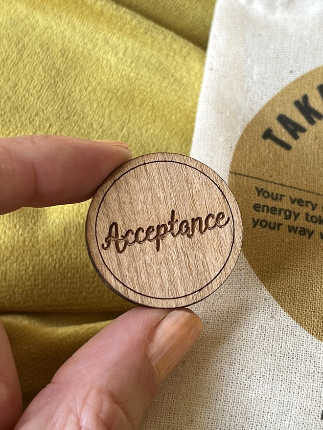 Close up shot of a token which reads "Acceptance" being held by a index finger and thumb 