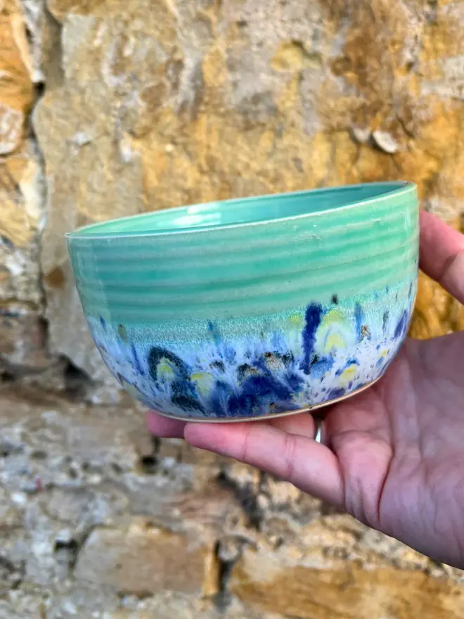 Shoreline Small Bowl, a colourful bowl held in front of a brick wall. 