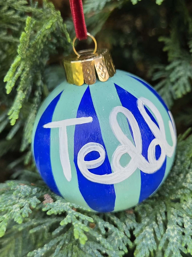 hand painted blue and mint stripe bauble with name personalisation, hanging on a christmas tree