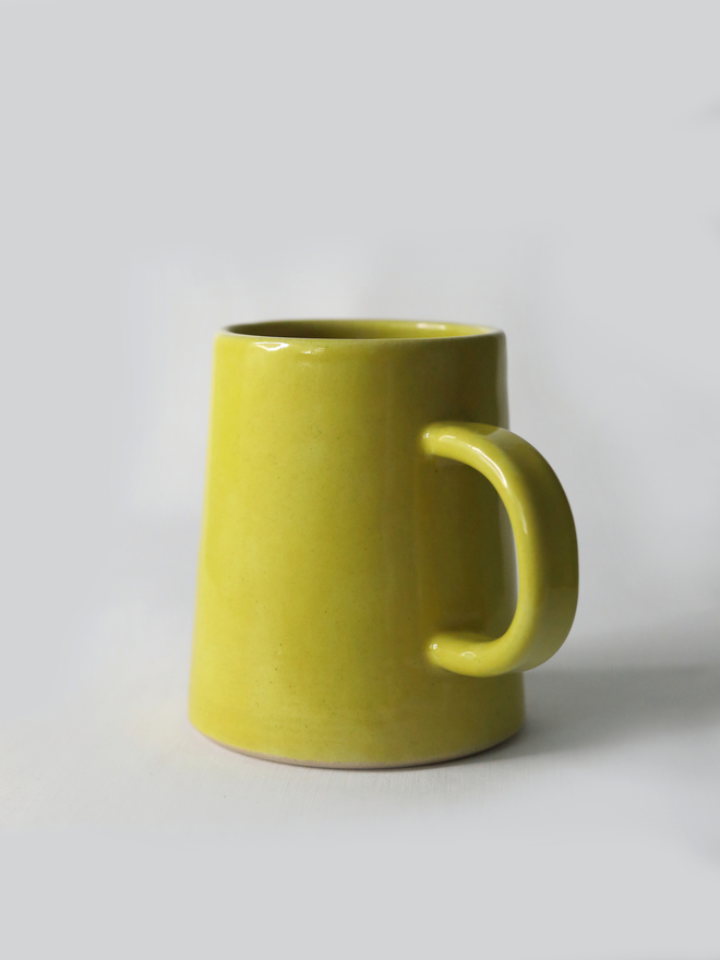 A handmade ceramic pint mug in sun yellow glaze with a chunky loop handle, photographed against a plain light grey background