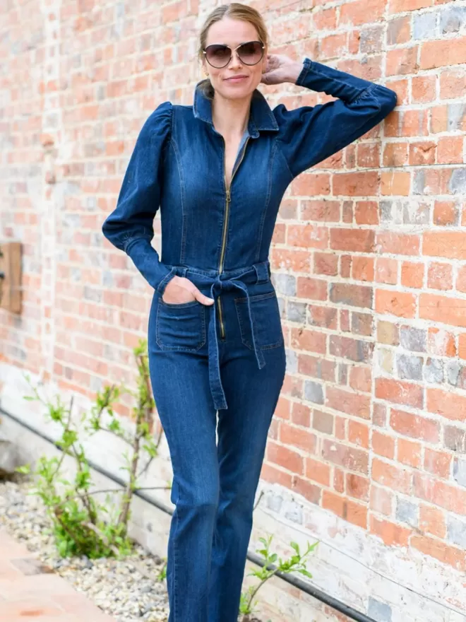 model wearing the bonnie denim jumpsuit leaning against a brick wall